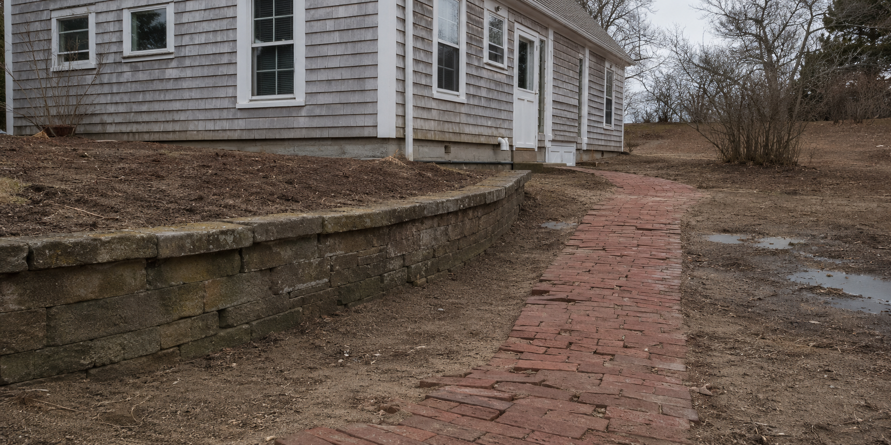 Retaining wall, uneven brick walkway and poor yard drainage before hardscape work in Cape Cod, MA