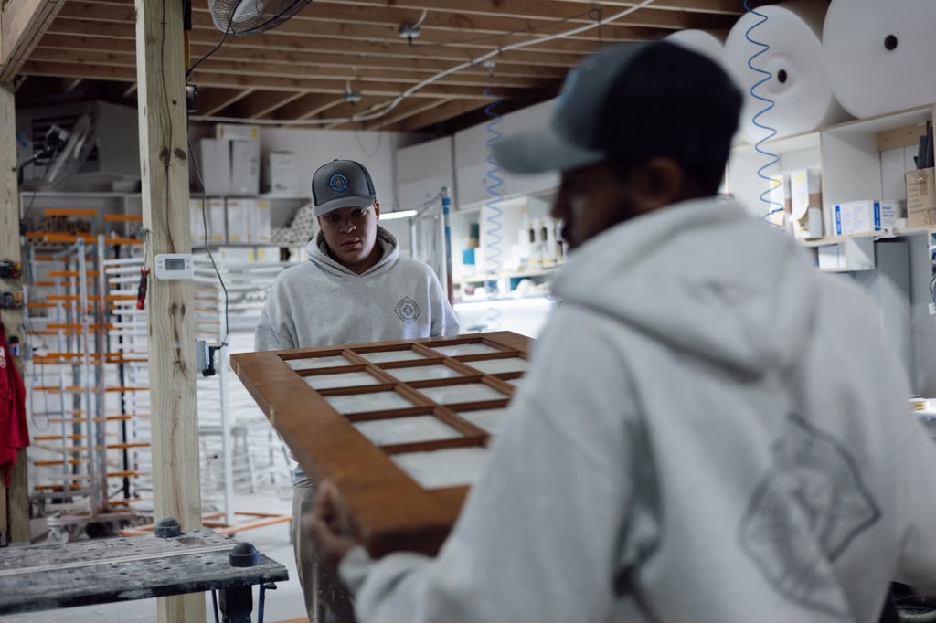 Woodworkers handling a finished cabinet door inside the Cape Cod shop